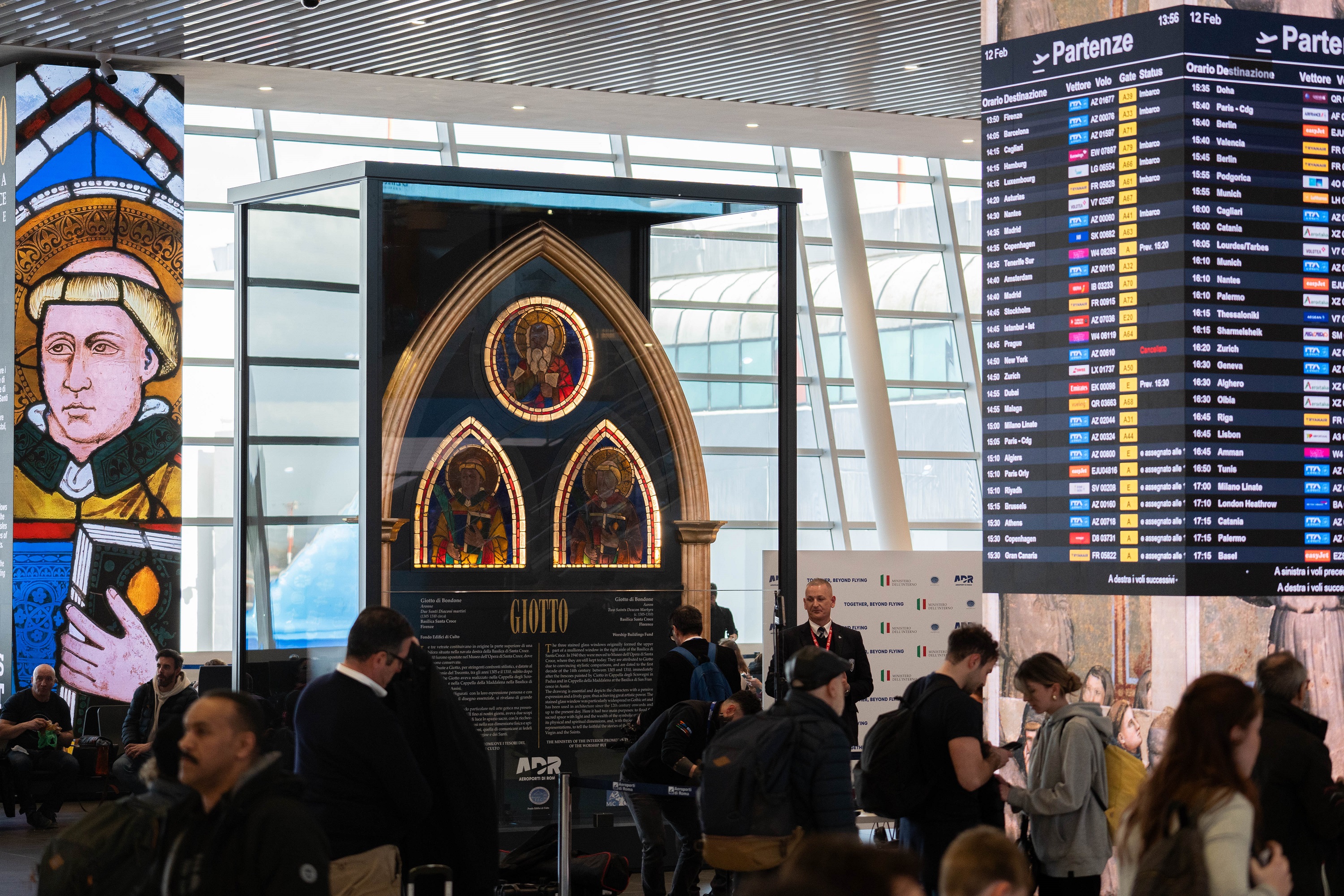 Art installation displaying medieval stained glass windows in Giotto style presented in a luminous frame inside the airport.